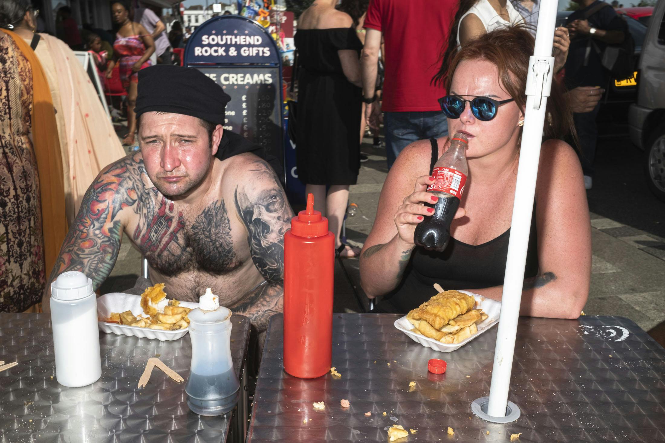 Man with tattoos and woman drinking coke eating fish and chips on Southend beach