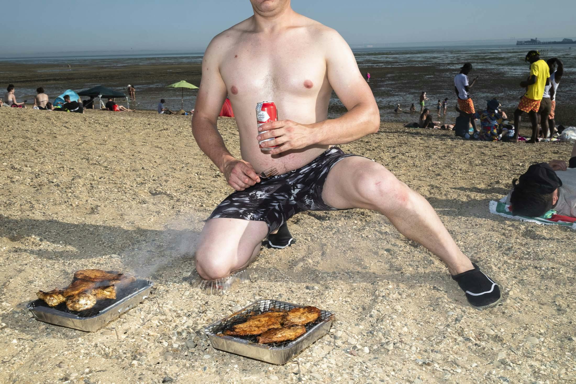 Shirtless man drinking Budweiser cooking meat on Southend beach
