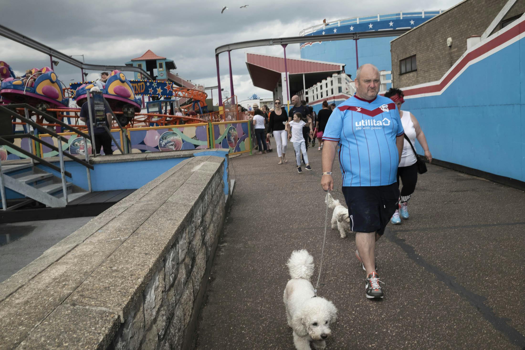 Man walking dog in amusement park wearing blue football soccer shirt that lines up with background