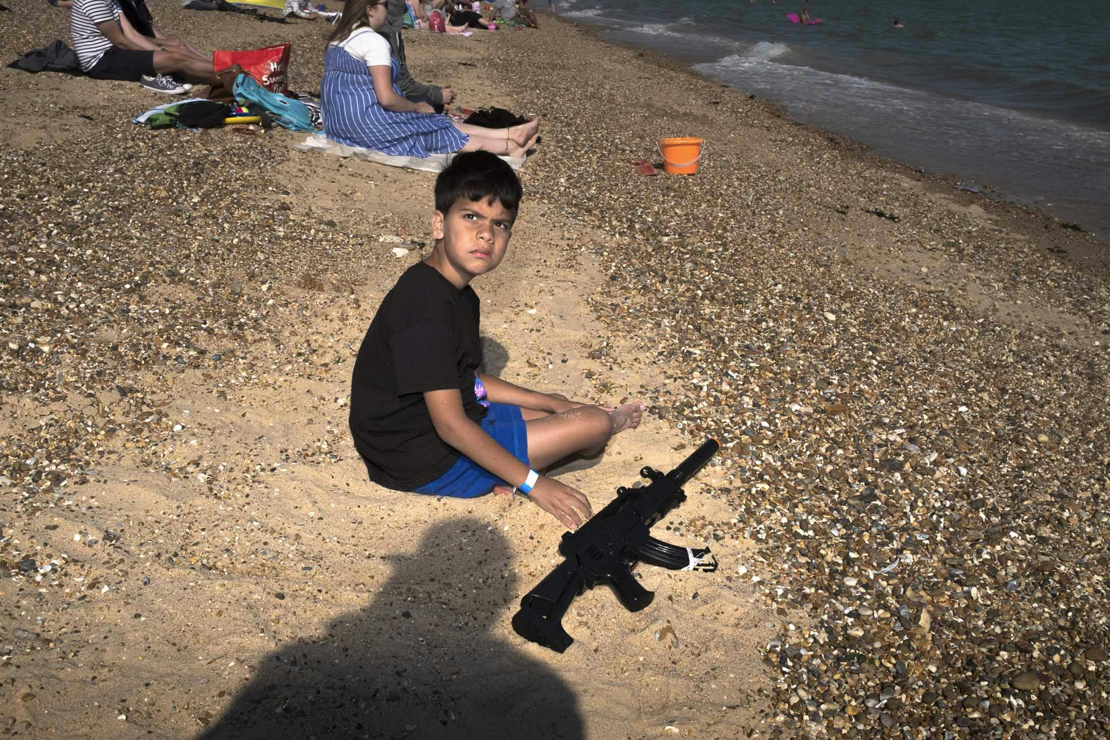 Boy sitting on beach at sunset with toy machine gun