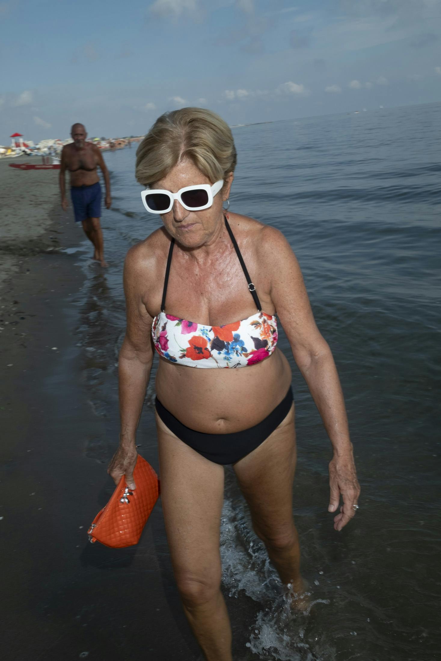Woman walking on shoreline with white sunglasses
