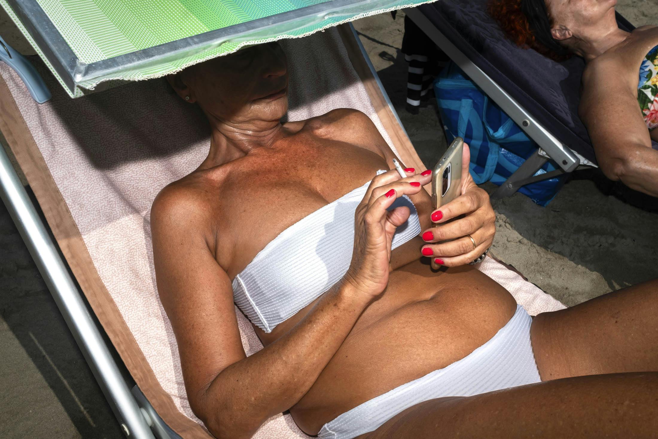 woman on sun lounger using phone and smoking