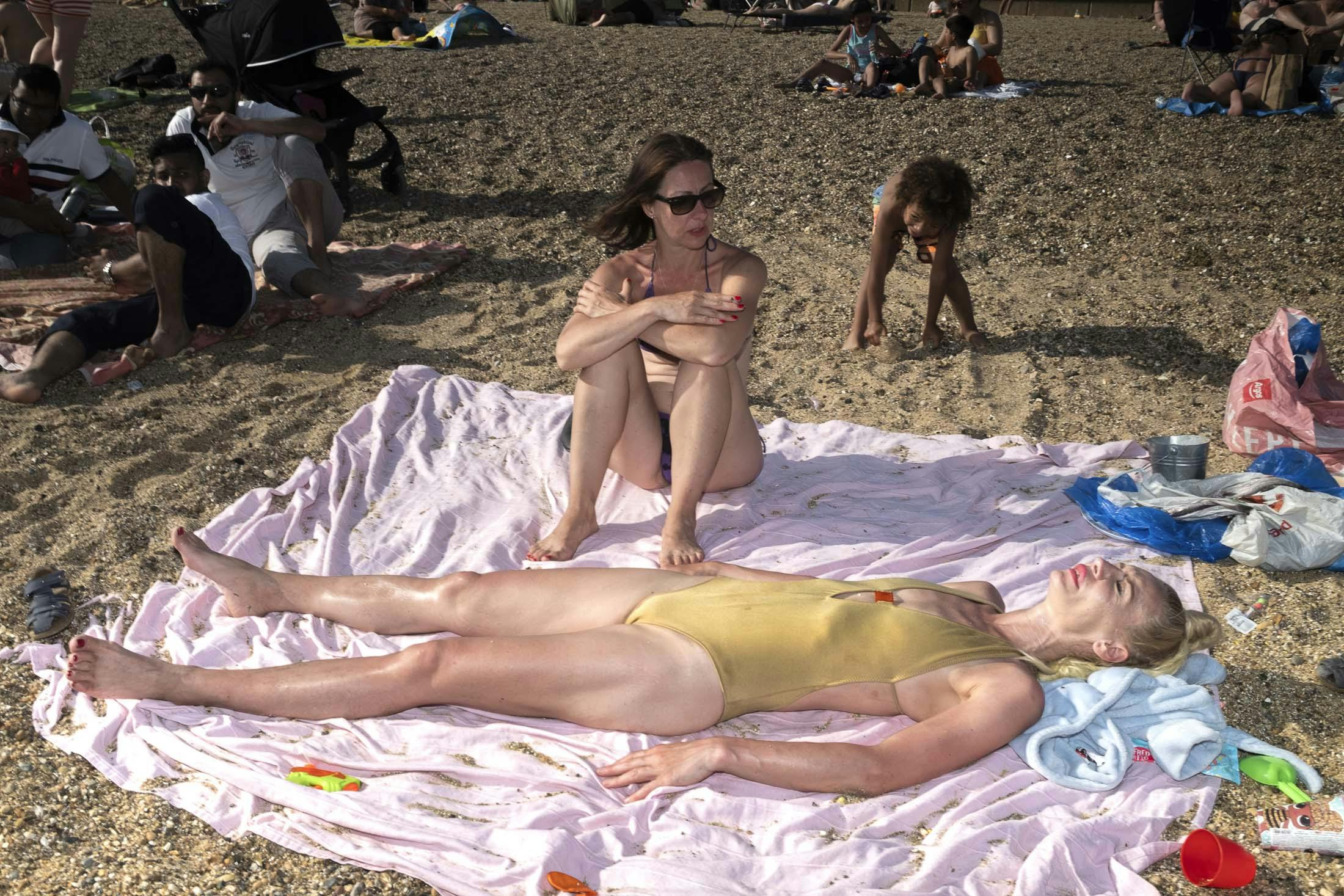 Woman sunbathing with gold swimsuit on pink towel with friend and child