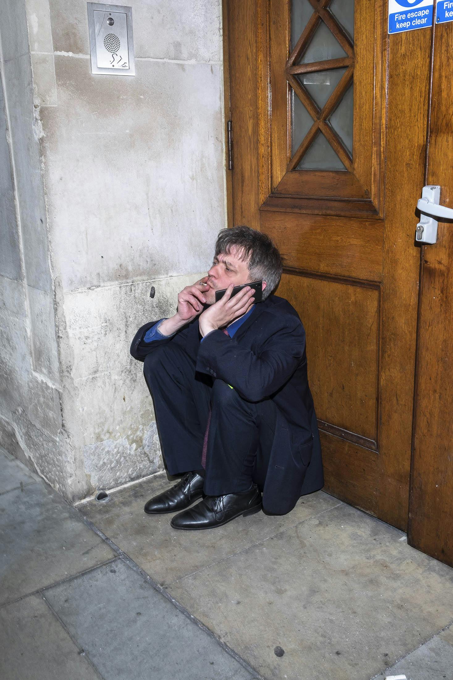 Business man wearing blue suit sat in doorway smoking and on phone