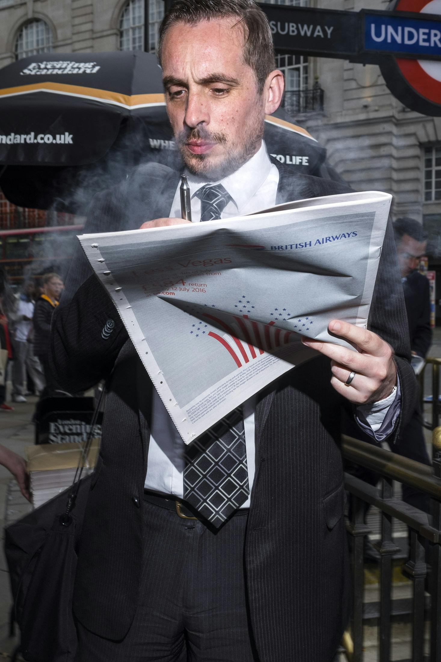 Busines man smoking vape in London reading newspaper 