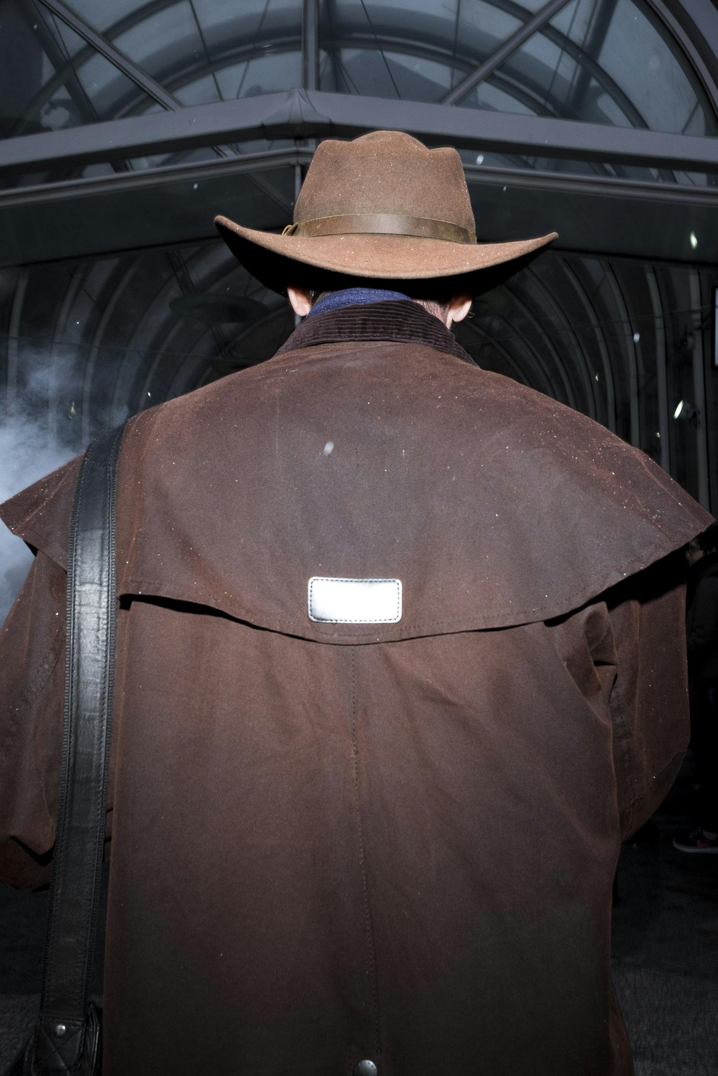 Man wearing brown mac and stetson entering Liverpool street station. 