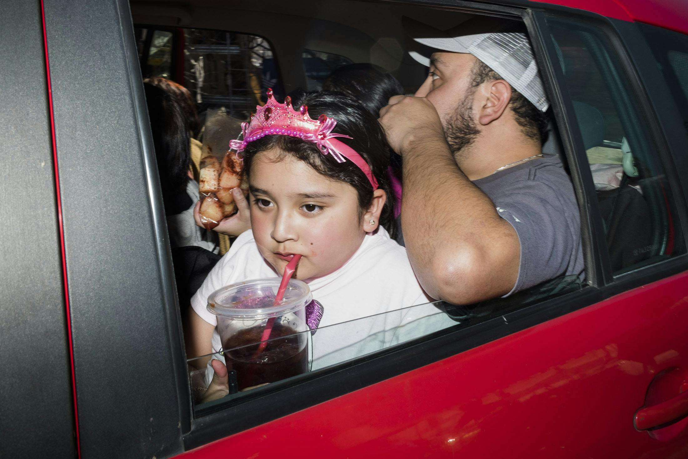Girl drinking coke through car window wearing a pink tiara 